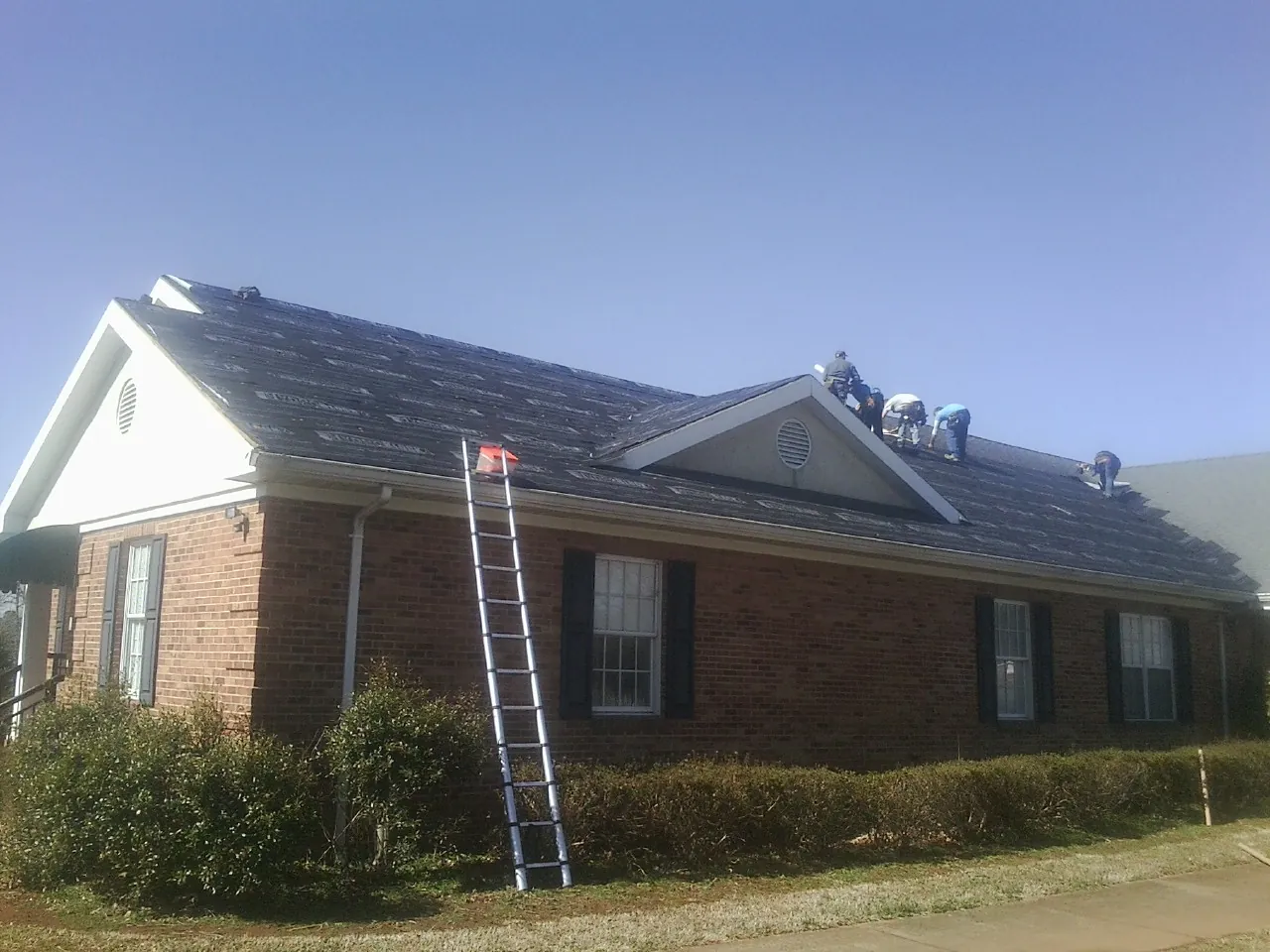 Crew tearing shingles off a brick ranch roof with a ladder set — Emergency Roof Repair work by our crew in Twain Harte