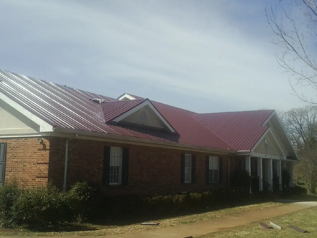 Red metal roof with gabled entries on a long brick building, from a Hail Damage Roof Repair job in Twain Harte