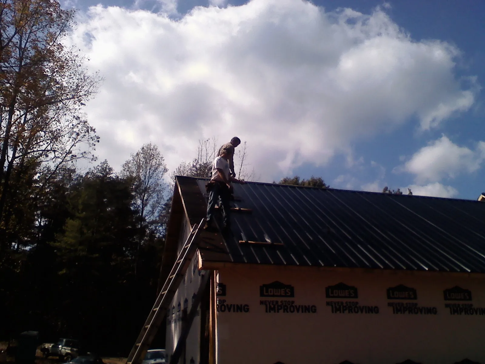 Roofer fastening dark metal panels high against a cloudy sky, from a Roof Inspection job in Twain Harte