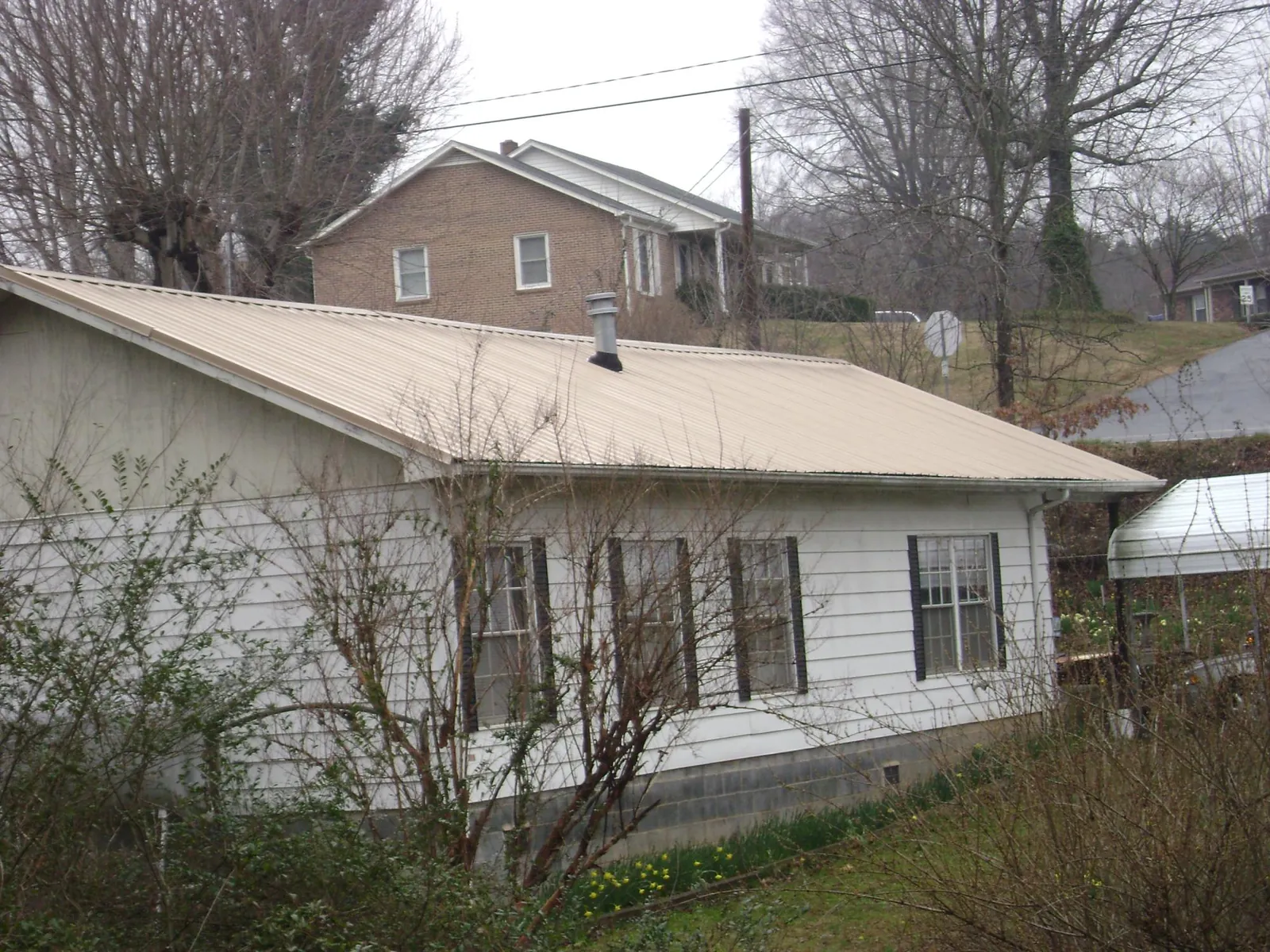 Tan metal roof on a white sided house set into a hillside — Commercial Roofing by Roofing Brothers in Twain Harte