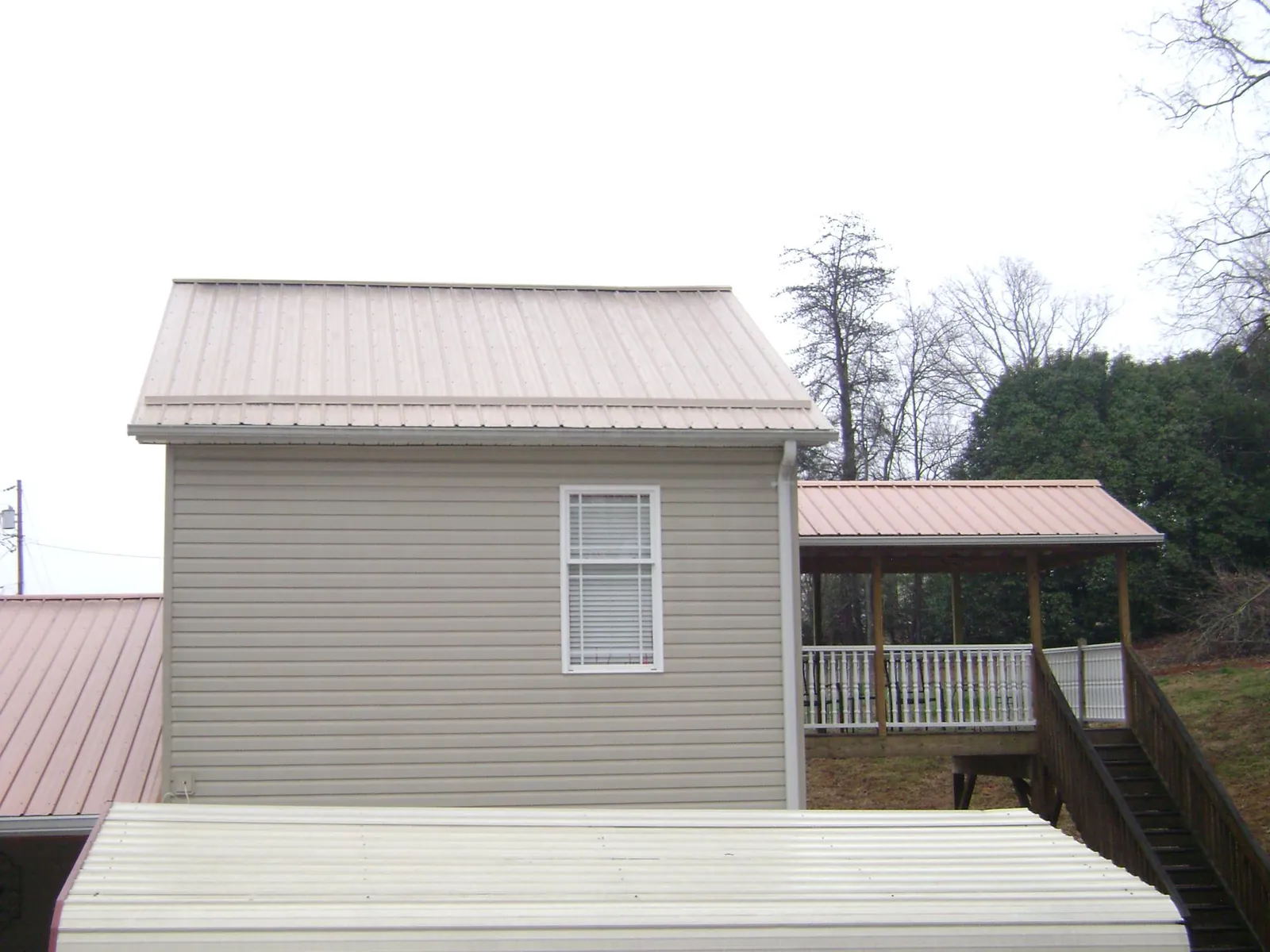 Tan metal roofs on a two story addition and attached porch, from a Roof Replacement job in Twain Harte